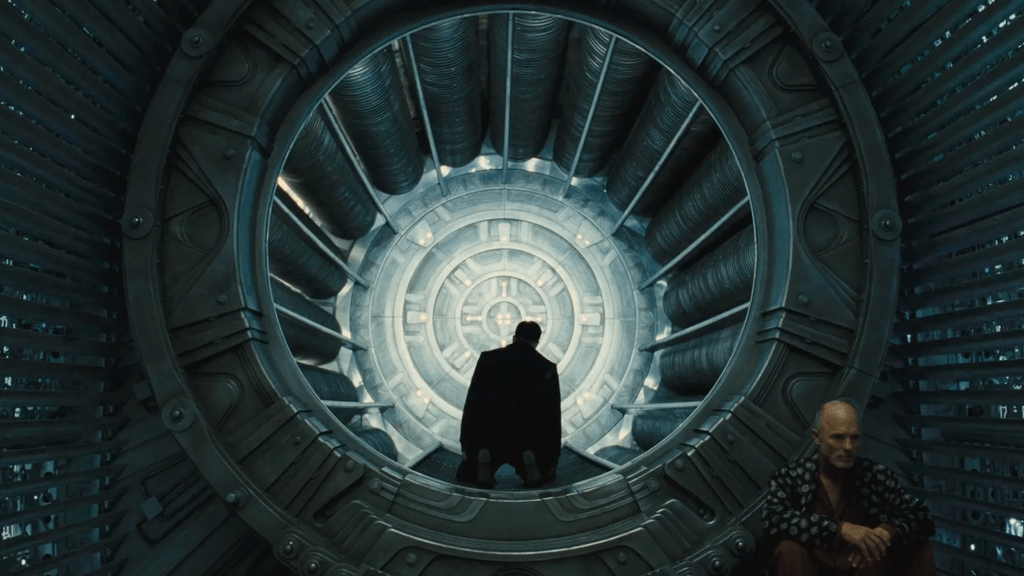 A silhouette of a person standing inside a circular futuristic structure, looking outward towards a spiral design, with another person seated in the foreground.
